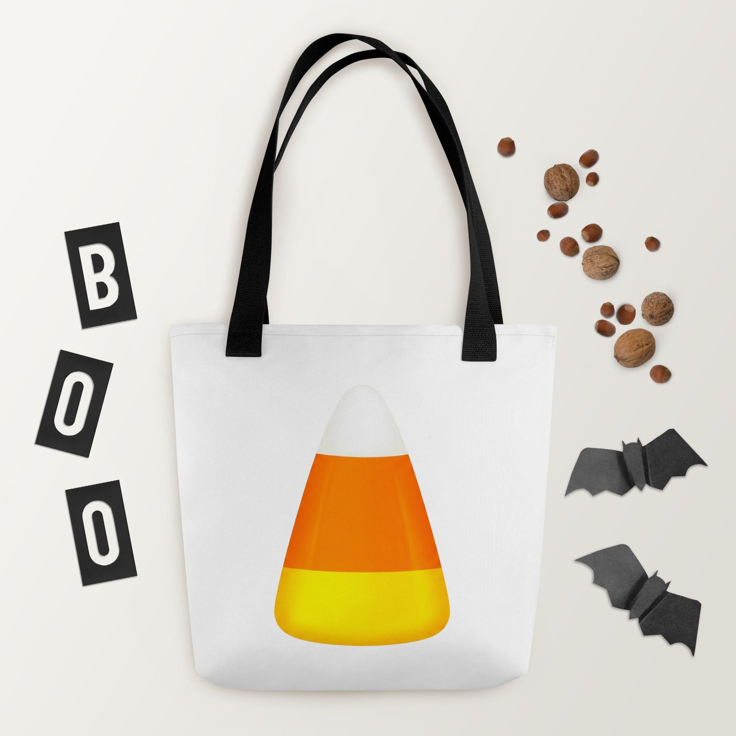 A white tote bag with black handles, featuring a large candy corn graphic