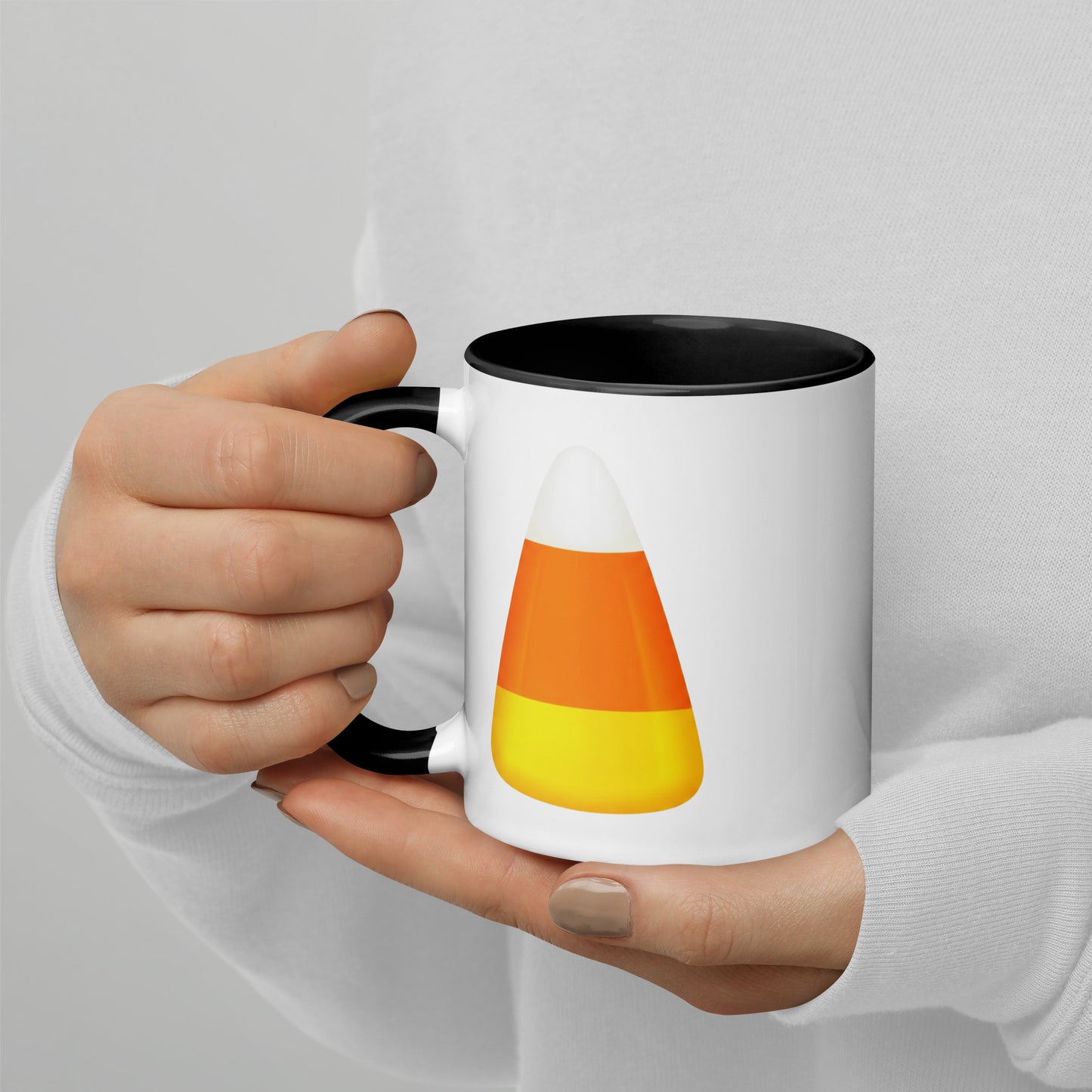 White mug with a black handle and interior. The mug features a printed candy corn graphic in orange, yellow, and white.