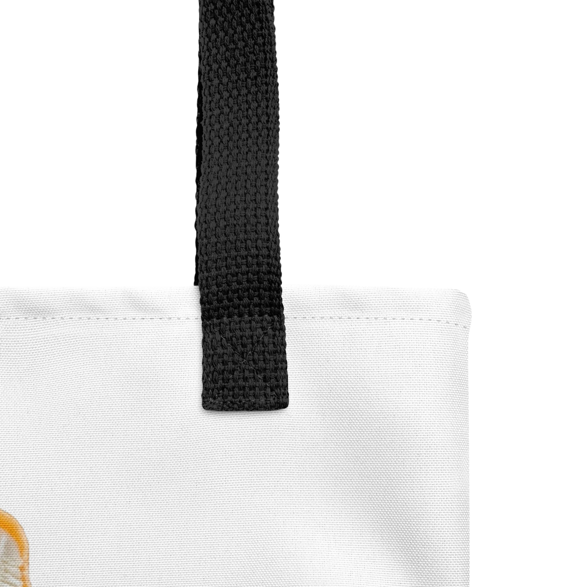 Close-up of a white tote bag with a thick black woven shoulder strap. Orange cream popsicle design.