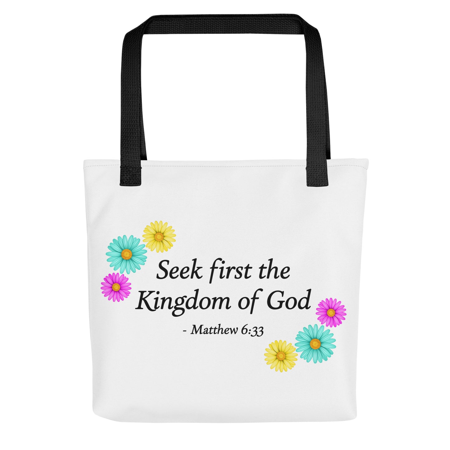 A white tote bag with black shoulder straps, featuring the printed text 'Seek first the Kingdom of God - Matthew 6:33' in black, decorated with colorful daisy flowers in yellow, teal, and pink.