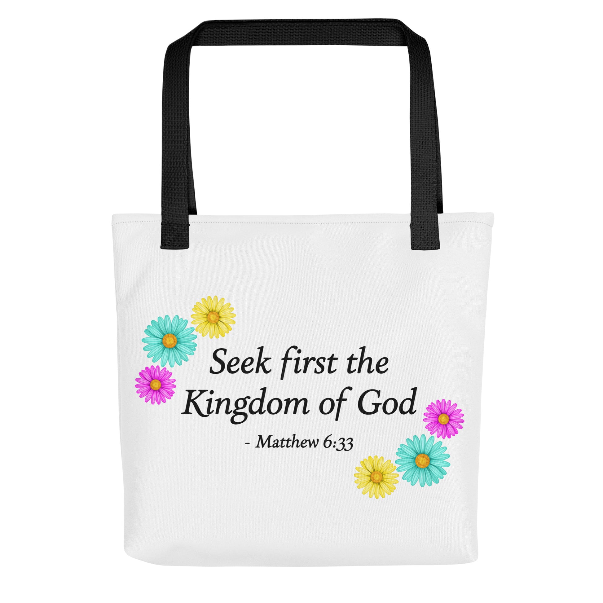 A white tote bag with black shoulder straps, featuring the printed text 'Seek first the Kingdom of God - Matthew 6:33' in black, decorated with colorful daisy flowers in yellow, teal, and pink.